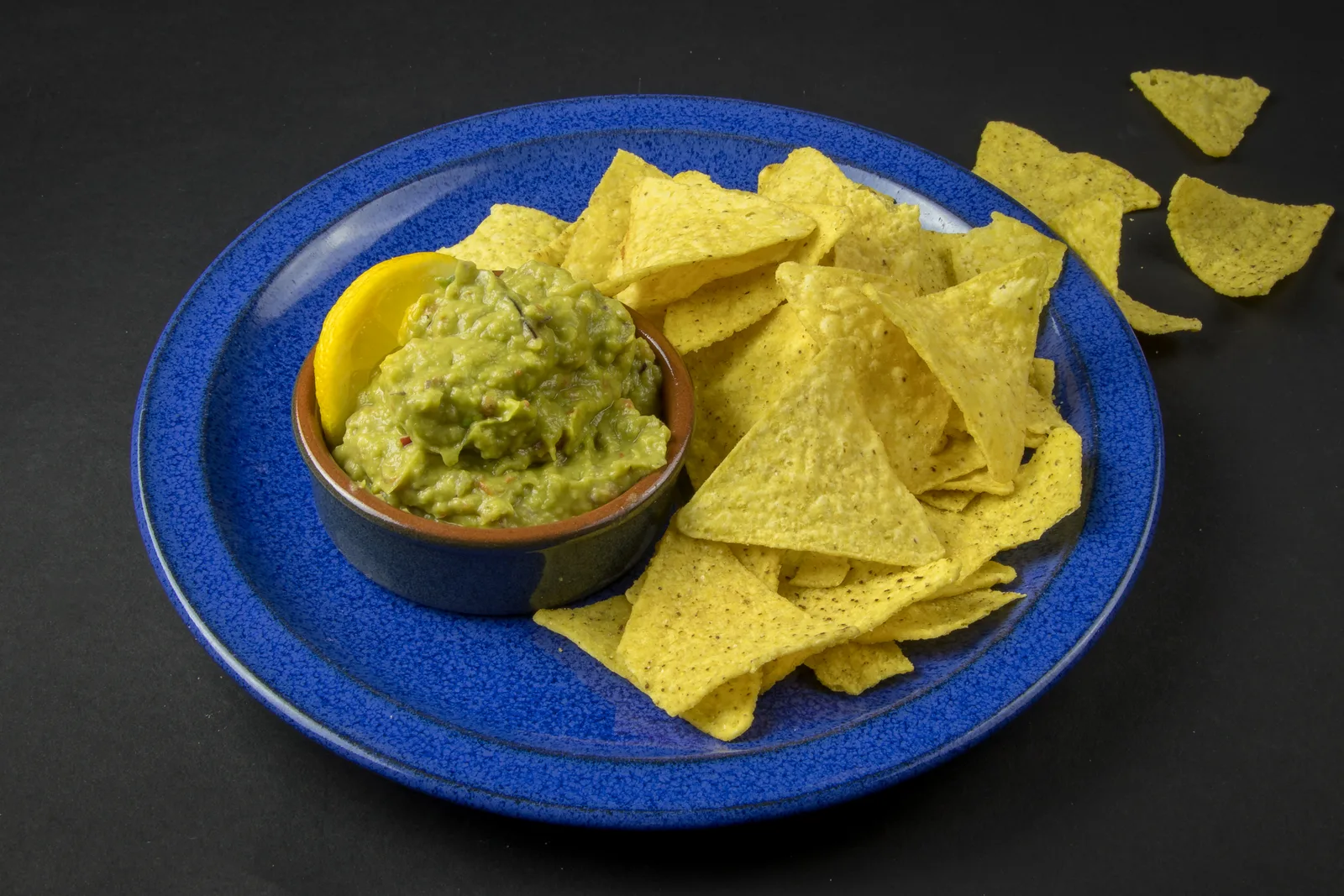 A bowl of guacamole beside tortilla chips on a blue plate